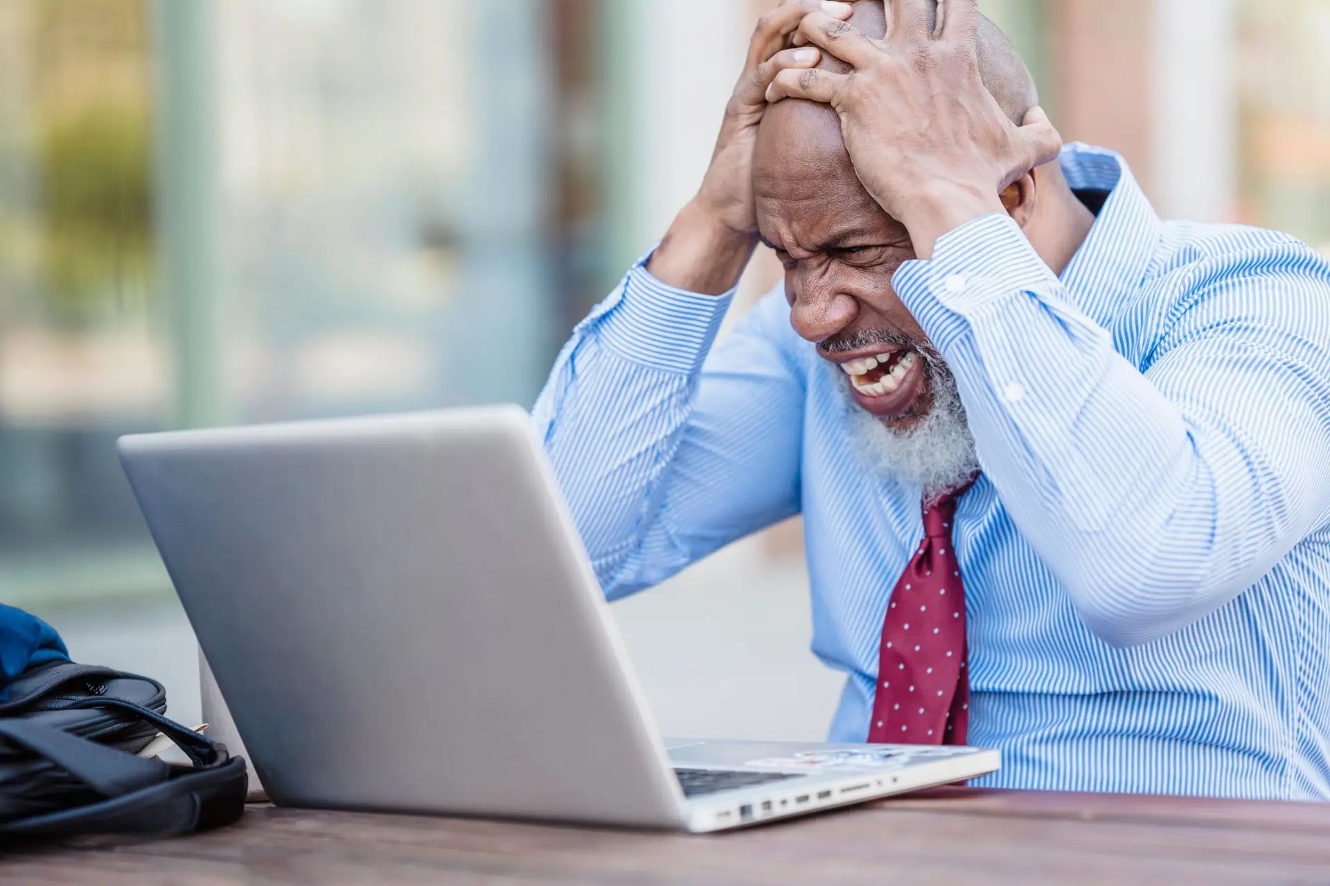 frustrated man, wearing a blue shirt and red tie, sitting at a laptop computer